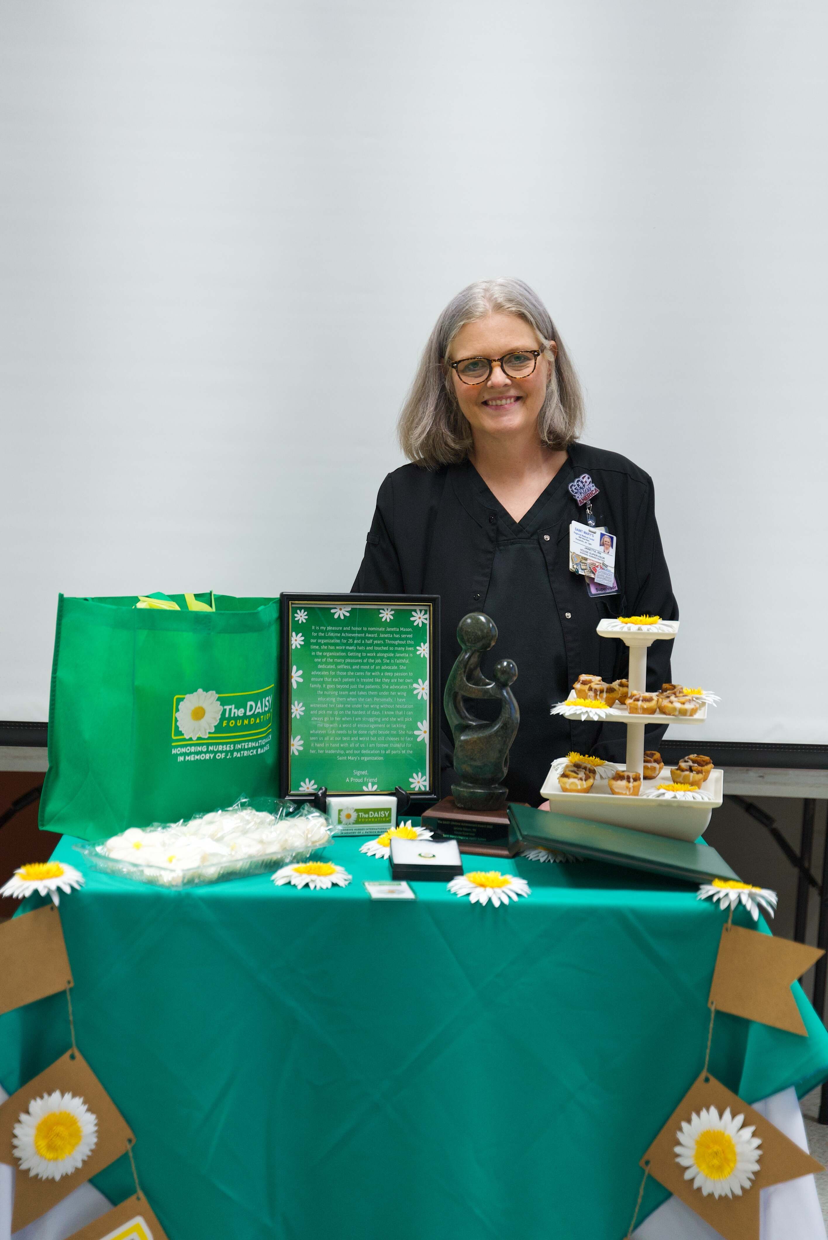 A Saint Mary’s nurse stands beside a DAISY Award display featuring a recognition plaque, award statue, daisies, treats and a DAISY Foundation gift bag. The nurse was honored for providing exceptional, compassionate patient care.