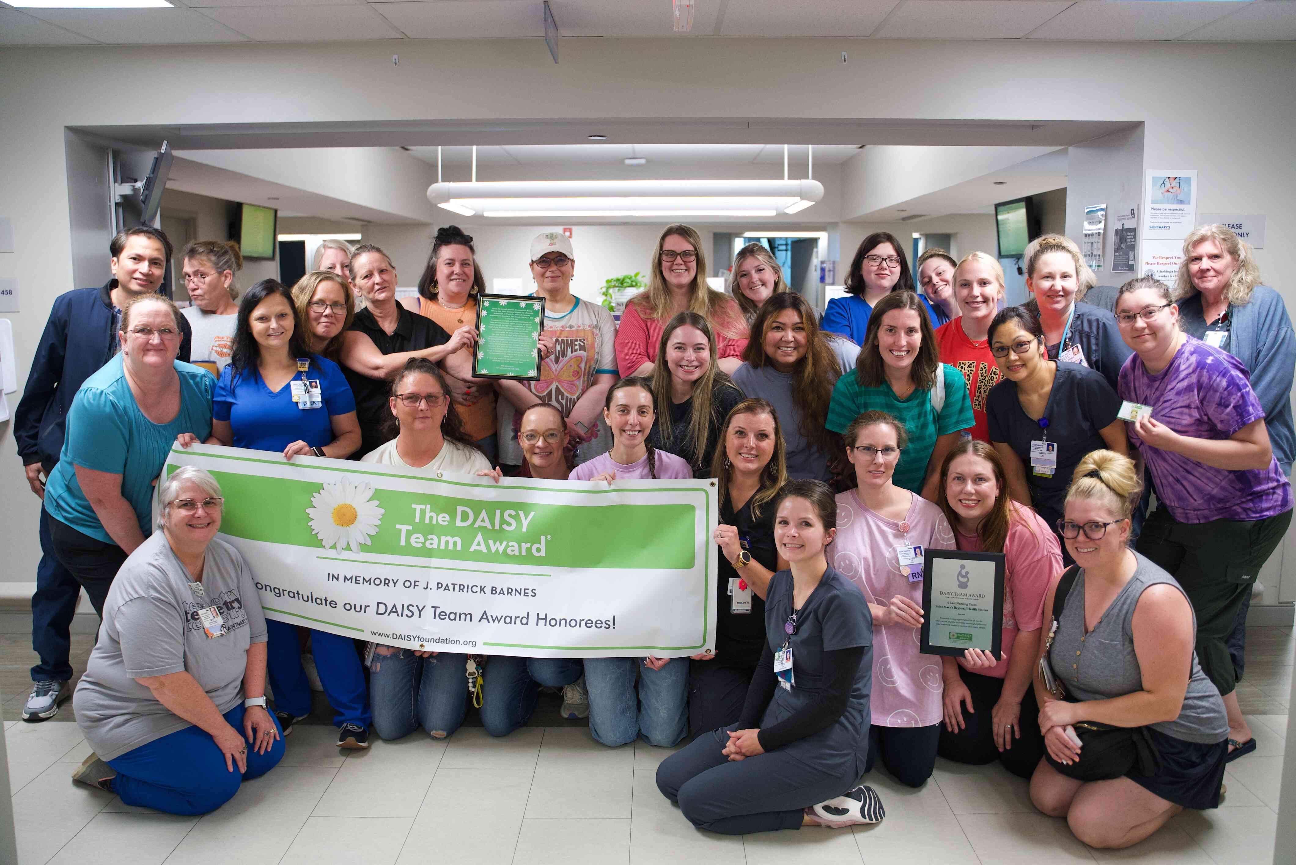 Saint Mary’s staff gather in a hospital unit holding a DAISY Team Award banner and recognition plaques. The team was honored for outstanding teamwork and compassionate patient care as part of the DAISY Award program.